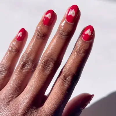 Human hand displaying red manicured nails with small decorative elements on each nail