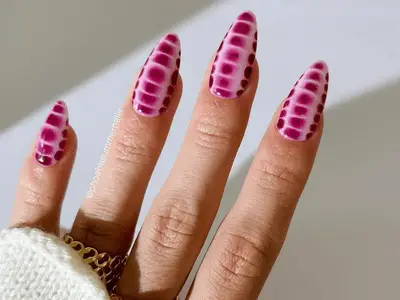 close up of pink crocodile print manicure against white background