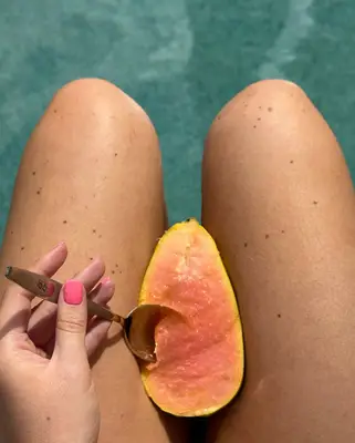 A hand wearing guava pink nail polish takes a spoon to a pink guava.