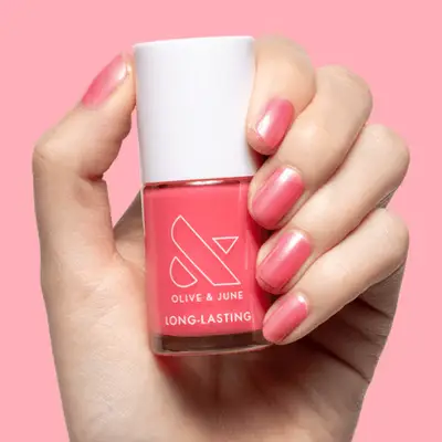 A hand showing pink nail polish with a bottle of 'Olive & June nail polish