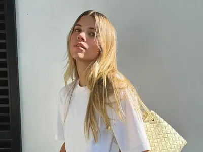 Sofia Grainge posing outdoors, wearing a white shirt and carrying a woven bag