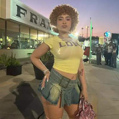 Ice Spice with curly red hair, denim mini skirt, balenciaga purse, and French nails