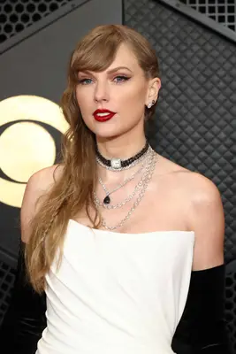 Taylor Swift attends the Grammys in a strapless white dress and damp-looking wavy hair with a small braid detail, plus red lips.