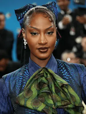 Tems at the 2025 Met Gala wearing skinny brows and glossy cherry cola lip combo