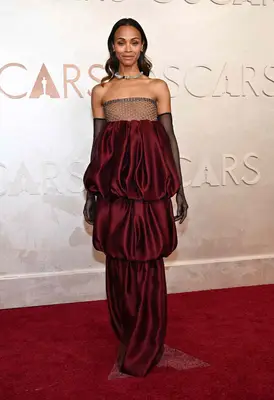 Zoe Saldana wears a tiered burgundy gown with sparkly top and opera gloves to the 2025 Oscars