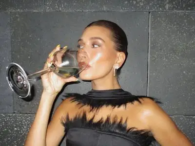 Hailey Bieber sips out of a wine glass.
