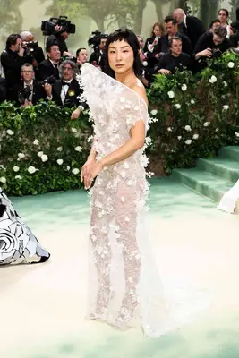 Greta Lee wears a sheer white gown with floral accents and structured neckline to the 2024 Met Gala