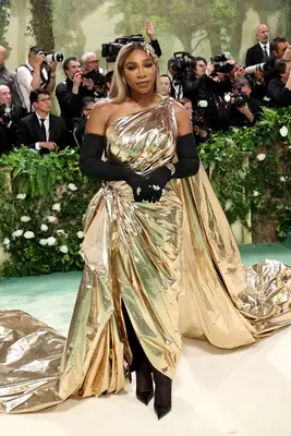 Serena Williams wears a metallic gold gown with a twisted shoulder into cape and black opera gloves to the 2024 Met Gala