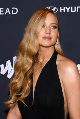 Jennifer Lawrence with her hair in a side-part wearing a glossy lip, bronzey eyeshadow, and a stack of earrings.