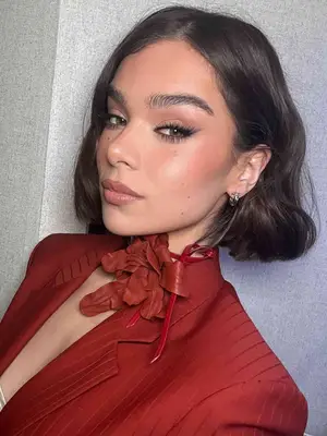Hailee Steinfeld with a bob hairstyle, red outfit, and neutral glam makeup look