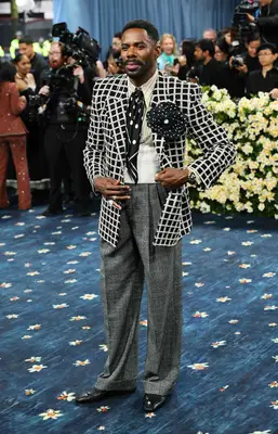 Colman Domingo wears a black and white plaid jacket, black and white polka dot silk tie and corsage, gray slacks, black shoes, and pinstriped button-down to the 2025 Met Gala