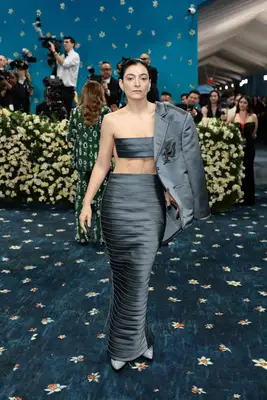 Lorde wears a gray crop top and mermaid maxi skirt set with half suit jacket to the 2025 Met Gala