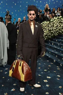 Bad Bunny wears a brown suit with gloves and nestlike hat and oversized leather bag to the 2025 Met Gala