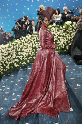Jodie Turner-Smith wears an oxblood leather dramatic trench with raffia top hat to the 2025 Met Gala