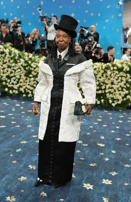 Whoopi Goldberg wears an hourglass black and white tailored suit gown and top hat with netting to the 2025 Met Gala