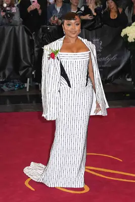 Quinta Brunson wears a black and white pinstriped gown and suit jacket with red rose corsage to the 2025 Met Gala