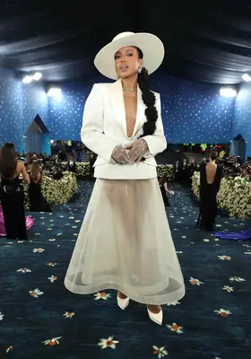 Kerry Washington wears a cream structured blazer with plunge neckline, sheer skirt, pumps, and wide brim hat to the 2025 Met Gala