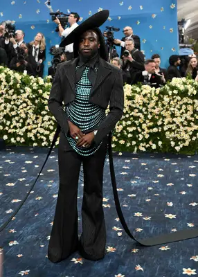 Shaboozey wears a black suit with turquoise beading and a tilted fascinator to the 2025 Met Gala