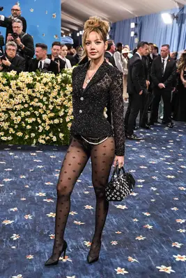 Lisa from Blackpink wears a tailored black Louis Vuitton jacket, bodysuit, patterned tights, bowling bag, heels, pearls, and pendant necklace to the 2025 Met Gala