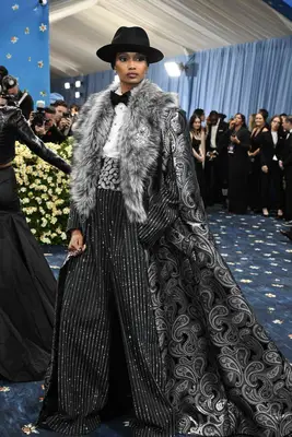 Ugbad Abdi wears a fur-trim coat, pinstriped jacket and pants, patterned cummerbund, and white shirt with black bow tie to the 2025 Met Gala