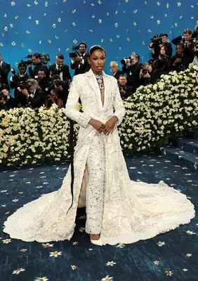 Coco Jones wears a white embroidered jacket with train and trousers paired with statement necklace to the 2025 Met Gala