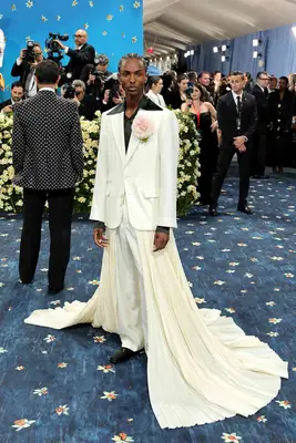 Christian Latchman wears a white jacket, pants, pleated train, and pastel pink corsage to the 2025 Met Gala