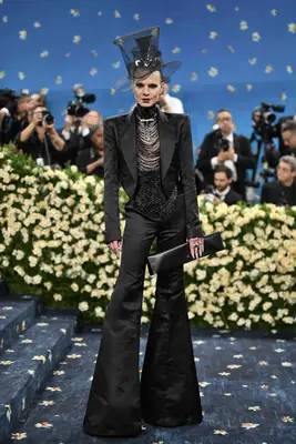 Jordan Roth wears a black suit with bell bottom flares, sparkly beading, and sheer top hat to the 2025 Met Gala