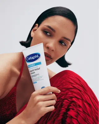 Nara Smith in a red dress holding moisturizer bottle