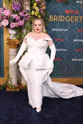 Nicola Coughlan wearing a bold red lip and off-the-shoulder white gown, gloves, and shoes. 
