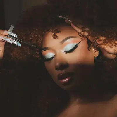 Megan Thee Stallion with 90s blue eyeshadow, clear lip gloss, and matching blue nails with floral designs