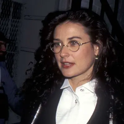 Demi Moore with curly hair, round glasses and neutral glossy lip.