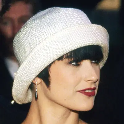 Demi Moore with a white bucket hat, blunt bangs, and a dark red lip. 