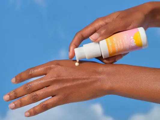 person applying sunscreen to back of hand against sky background