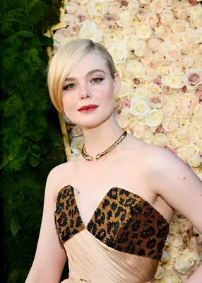 Elle Fanning poses at the Golden Globes in a strapless dress with a leopard print bodice, a collar necklace, and red lipstick.