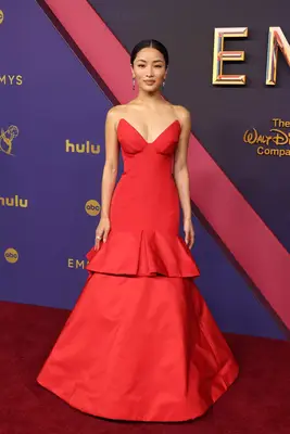 Anna Sawai wears a red Vera Wang gown with sharp sweetheart neckline and tiered ruffle waist to the 2024 Emmy Awards