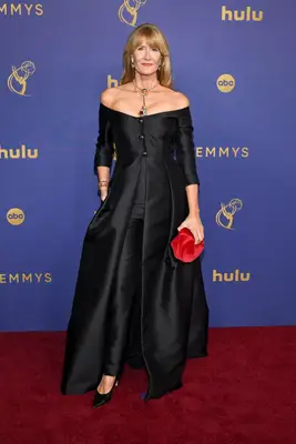 Laura Dern wears an off-the-shoulder long sleeved black gown with lariat necklace and red handbag