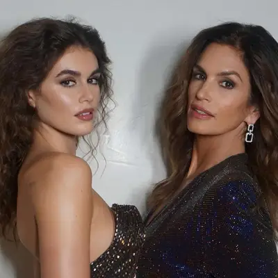 Kaia Gerber in a shiny black Celine dress paired with an 80s perm similar to the ones her mother, Cindy Crawford, used to wear while standing next to her