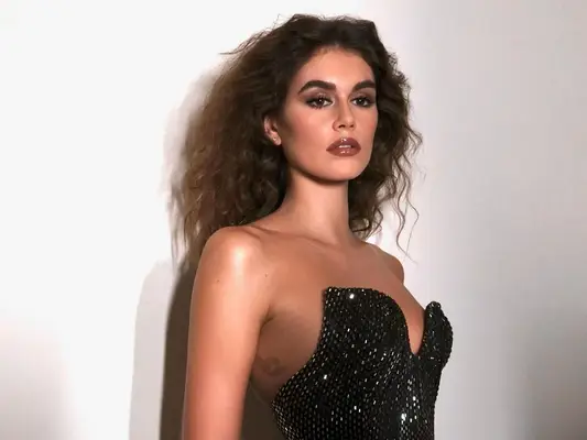 Kaia Gerber in a shiny black Celine dress paired with an 80s perm similar to the ones her mother, Cindy Crawford, used to wear