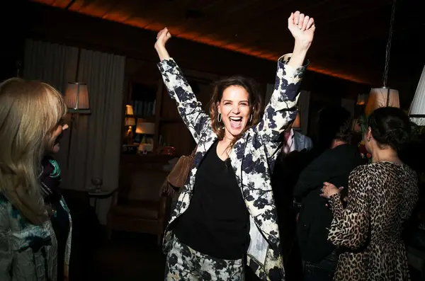 Katie Holmes throws her hands up in the air in excitement at an event celebrating Poker Face Season 2.
