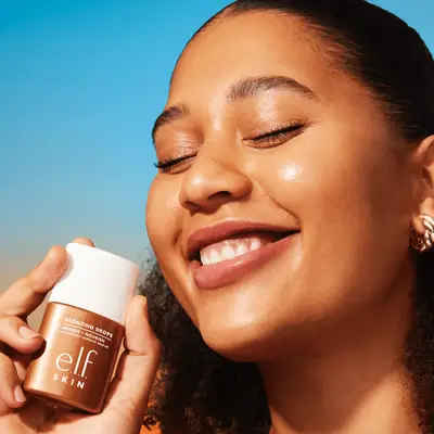 A close up of a model wearing and holding e.l.f. SKIN