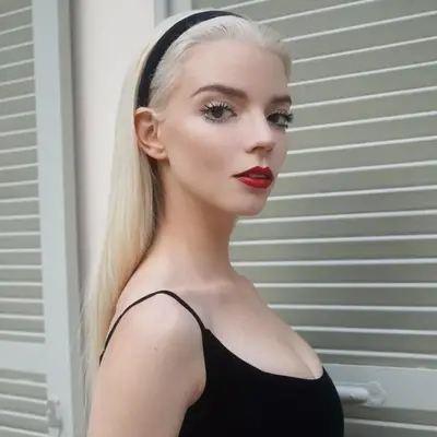 Anya Taylor-Joy in a black dress, black headband, red lipstick, and doll lashes