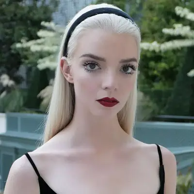 Anya Taylor joy in a black dress, black headband, doll lashes, and red lipstick