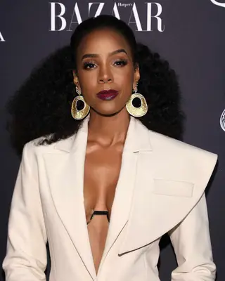 Kelly Rowland attends an NYC event in 2018 wearing a sculpted blazer, dark lip, natural hair and large earrings