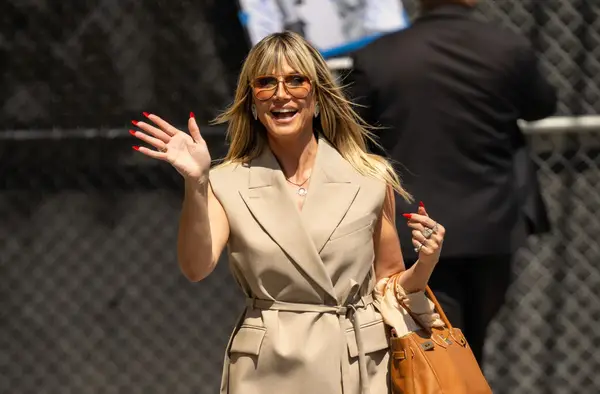 Heidi Klum waves at the camera while showing off her choppy bangs.