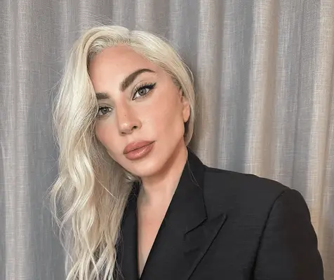 Lady Gaga with blonde hair in a side-part hairstyle. 