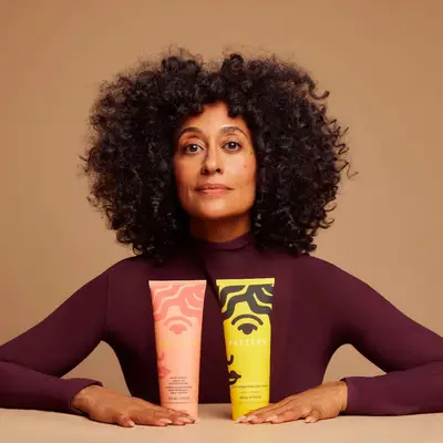 Tracee Ellis Ross sitting at a table with two products from her hair care brand, Pattern Beauty.