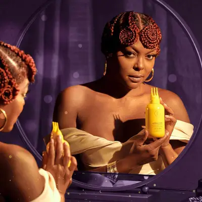 Tajari P. Henson looking in the mirror holding her scalp treatment.