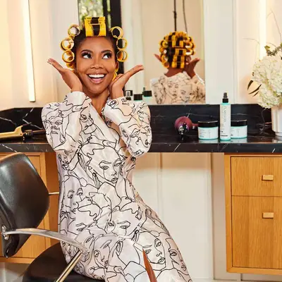 Gabrielle Union sitting in a salon chair with curlers in her hair and smiling.