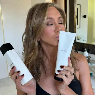 Jennifer Aniston holding two products from her haircare line and pretending to give the bottle a kiss.
