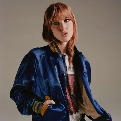 Hayley Williams posing for a portrait with a blue bomber jacket. 